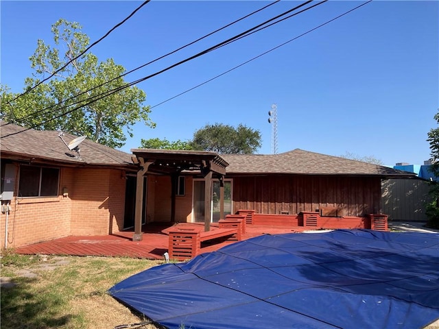 back of property featuring brick siding, a fenced in pool, a wooden deck, and a shingled roof