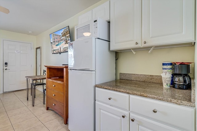 kitchen with white cabinetry, light tile patterned floors, white appliances, and stone counters