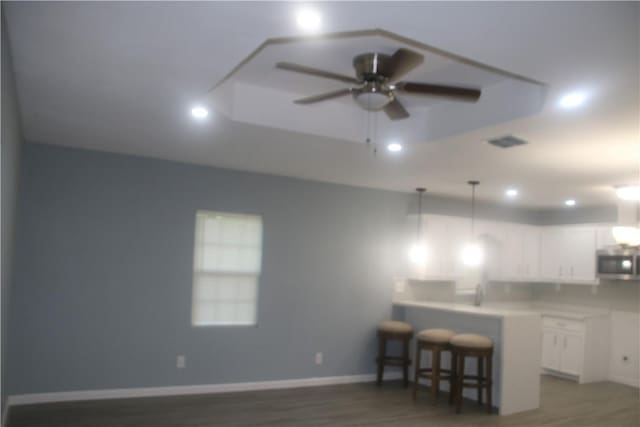 kitchen featuring white cabinets, hanging light fixtures, ceiling fan, a kitchen bar, and kitchen peninsula