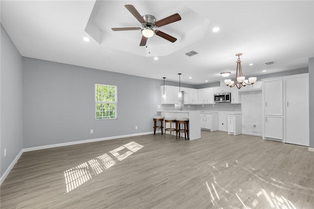 unfurnished living room with a raised ceiling, light hardwood / wood-style flooring, and ceiling fan with notable chandelier