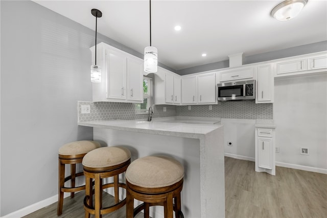 kitchen featuring a breakfast bar area, kitchen peninsula, white cabinets, and hanging light fixtures