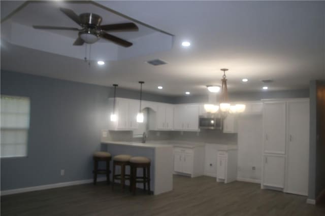 kitchen featuring kitchen peninsula, dark hardwood / wood-style flooring, white cabinets, and hanging light fixtures