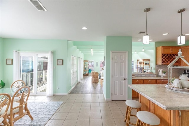 kitchen with a kitchen breakfast bar, backsplash, tile countertops, pendant lighting, and light tile patterned floors