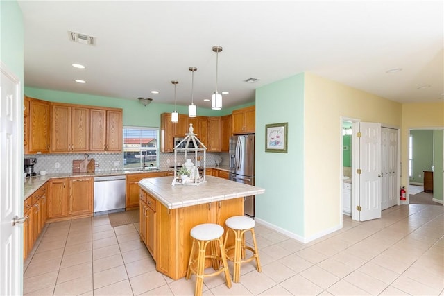 kitchen with a center island, backsplash, pendant lighting, a breakfast bar area, and appliances with stainless steel finishes