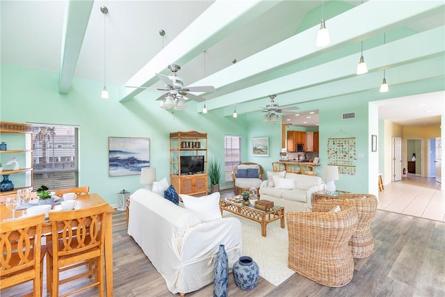 living room with beam ceiling, a wealth of natural light, a high ceiling, and hardwood / wood-style floors