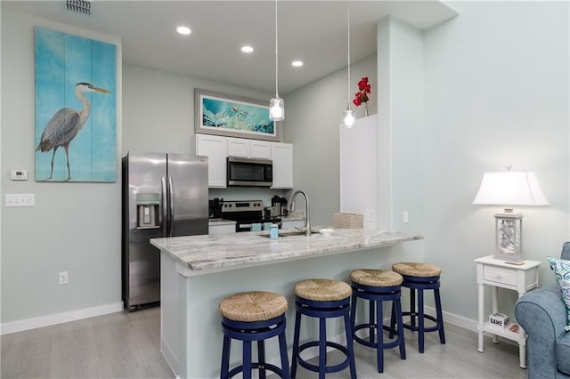 kitchen with a kitchen bar, stainless steel appliances, sink, decorative light fixtures, and white cabinets