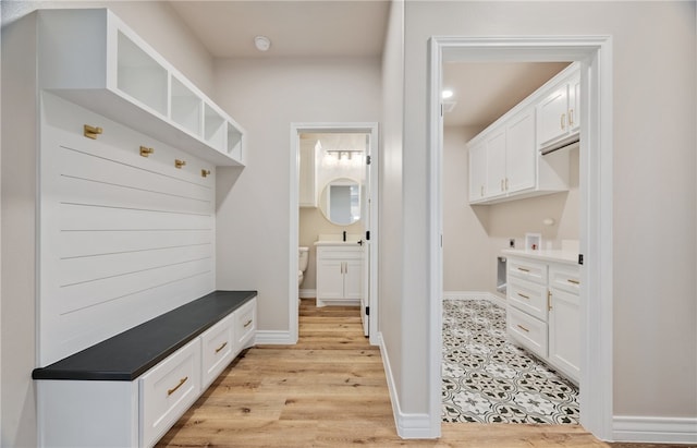 mudroom featuring light wood-type flooring, a sink, and baseboards