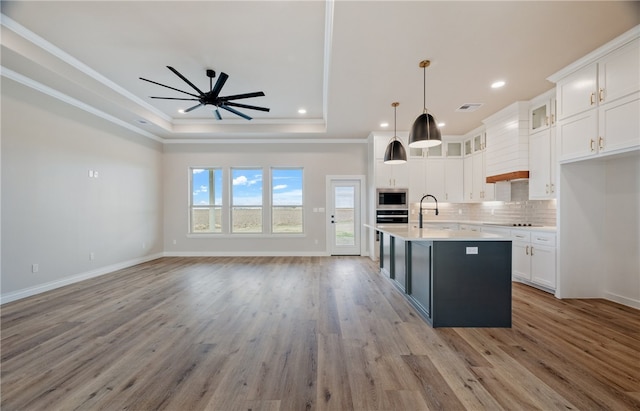 kitchen with white cabinets, an island with sink, stainless steel microwave, open floor plan, and light countertops