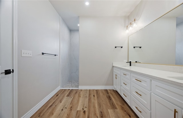 bathroom featuring a marble finish shower, double vanity, a sink, wood finished floors, and baseboards