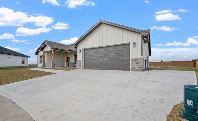 modern farmhouse style home with a garage, concrete driveway, stone siding, fence, and board and batten siding