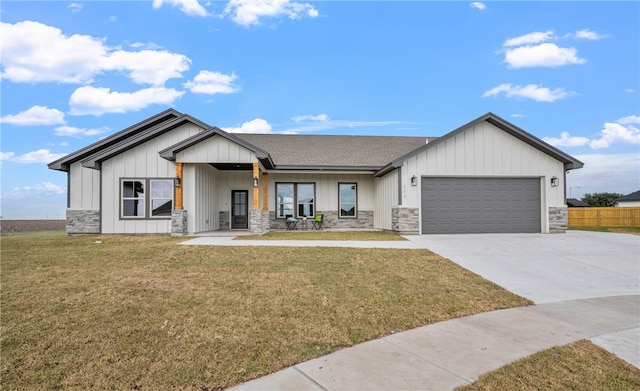 view of front of home with an attached garage, stone siding, concrete driveway, and a front yard