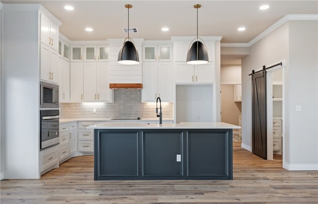 kitchen featuring a center island with sink, light countertops, a barn door, glass insert cabinets, and white cabinets