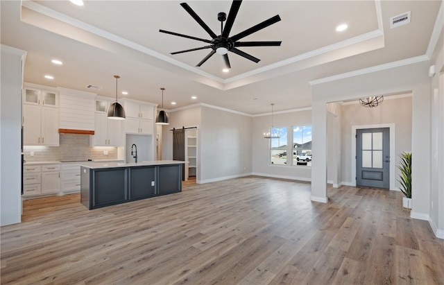 kitchen featuring a barn door, a raised ceiling, open floor plan, light countertops, and white cabinetry