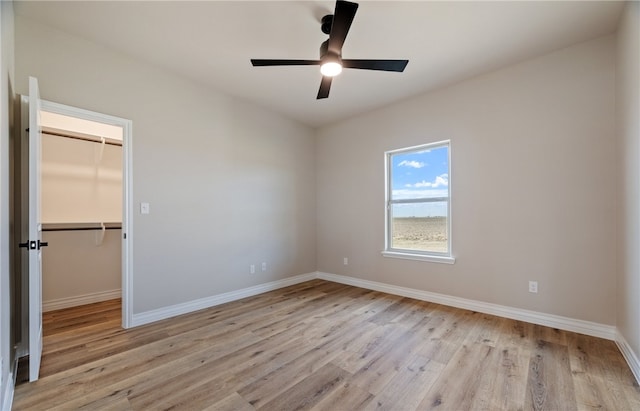 unfurnished bedroom with a closet, light wood-style flooring, baseboards, and a spacious closet