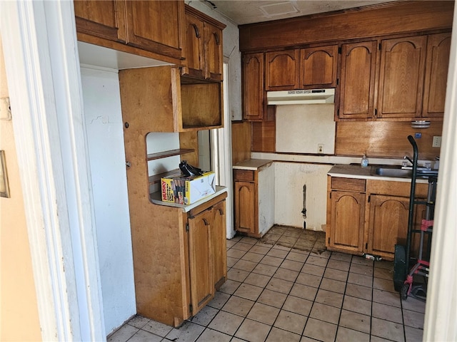 kitchen featuring under cabinet range hood, light countertops, light tile patterned floors, brown cabinets, and a sink