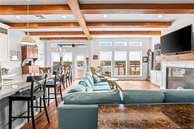 living area with an inviting chandelier, a glass covered fireplace, wood finished floors, and beamed ceiling