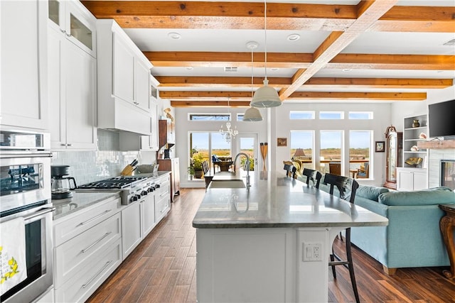 kitchen featuring beamed ceiling, open floor plan, dark wood-type flooring, a sink, and appliances with stainless steel finishes