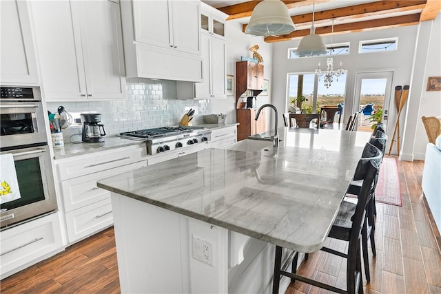 kitchen with a kitchen bar, a sink, backsplash, a notable chandelier, and stainless steel appliances
