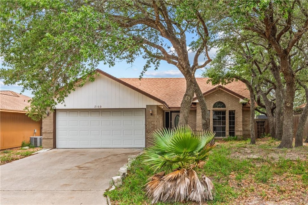 view of front of property with central AC, brick siding, a shingled roof, an attached garage, and driveway