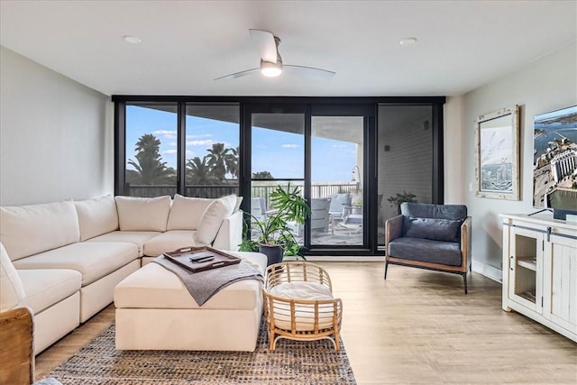 living room featuring ceiling fan, a wall of windows, and light hardwood / wood-style flooring