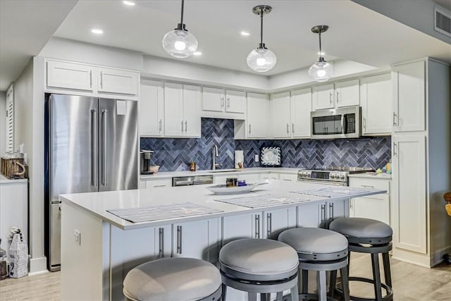 kitchen with a breakfast bar area, white cabinetry, a center island, appliances with stainless steel finishes, and pendant lighting