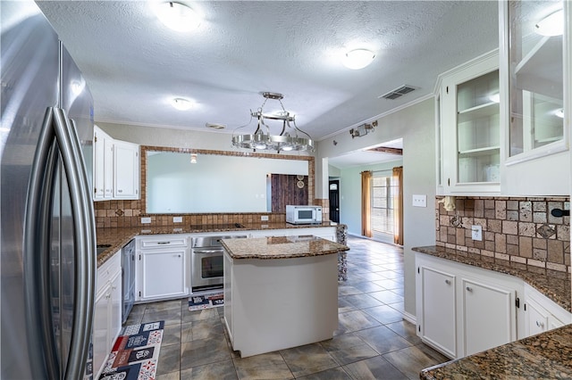 kitchen featuring white cabinets, crown molding, backsplash, appliances with stainless steel finishes, and dark stone countertops