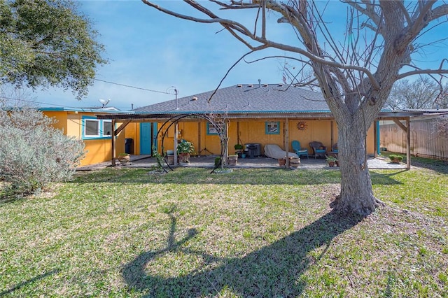 rear view of property featuring stucco siding, fence, a lawn, and a patio