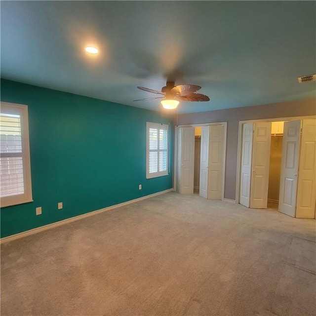 unfurnished bedroom featuring multiple closets, light colored carpet, visible vents, a ceiling fan, and baseboards