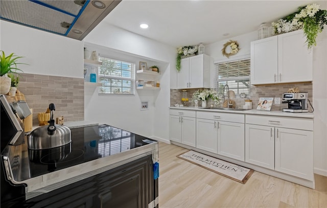 kitchen featuring open shelves, cooktop, light countertops, white cabinetry, and a sink