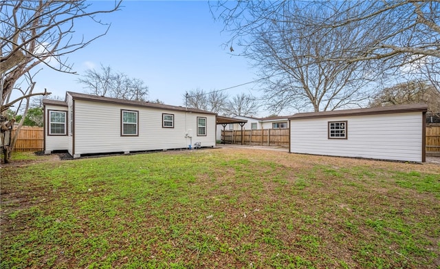 back of property featuring fence, a lawn, and an outbuilding