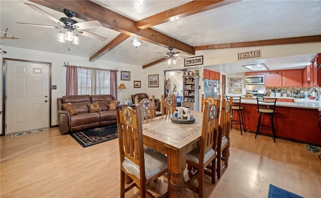 dining area featuring light wood finished floors, a textured ceiling, lofted ceiling with beams, and a ceiling fan