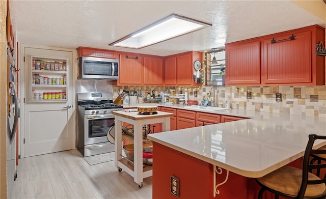 kitchen with a peninsula, a sink, light countertops, appliances with stainless steel finishes, and backsplash