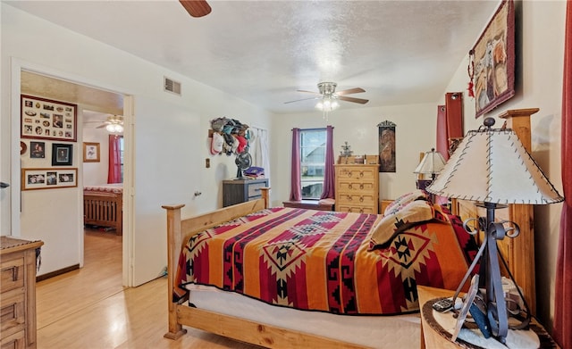 bedroom featuring visible vents, light wood-style flooring, a ceiling fan, ensuite bathroom, and a textured ceiling