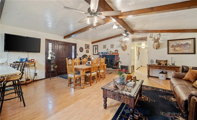 living area featuring visible vents, a ceiling fan, light wood-style floors, a fireplace, and vaulted ceiling with beams