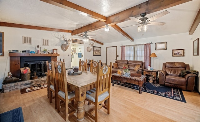 dining space with visible vents, ceiling fan, a brick fireplace, and light wood-style floors