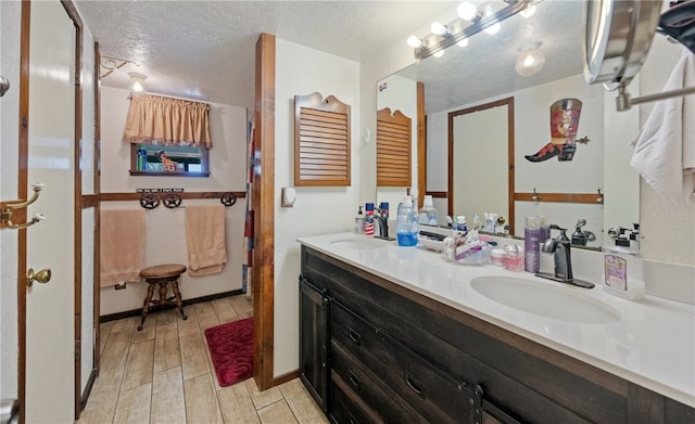 bathroom with a sink, wood finish floors, a textured ceiling, and double vanity