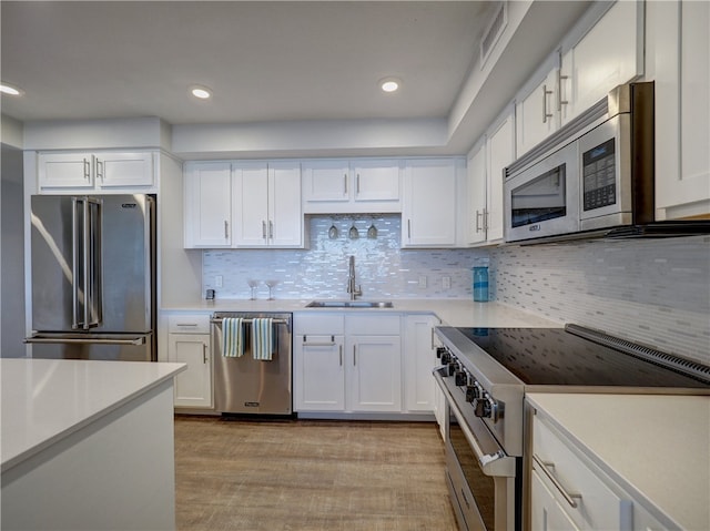 kitchen featuring high end appliances, sink, tasteful backsplash, white cabinetry, and light hardwood / wood-style flooring