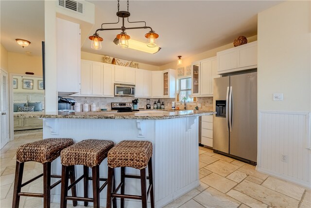 kitchen featuring tasteful backsplash, light stone counters, appliances with stainless steel finishes, white cabinets, and a breakfast bar area