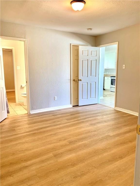 unfurnished room with a textured ceiling, light wood-type flooring, and baseboards