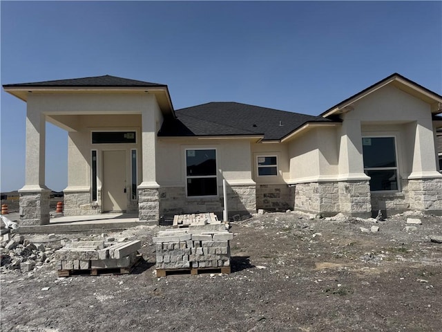 rear view of house with stucco siding, stone siding, and a shingled roof