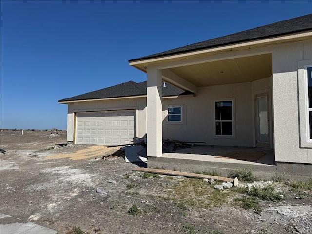 exterior space with a garage, roof with shingles, and stucco siding