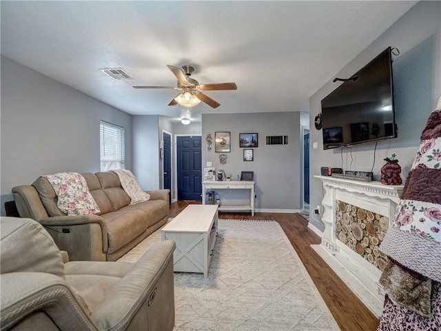 living room with wood finished floors, visible vents, a ceiling fan, and baseboards