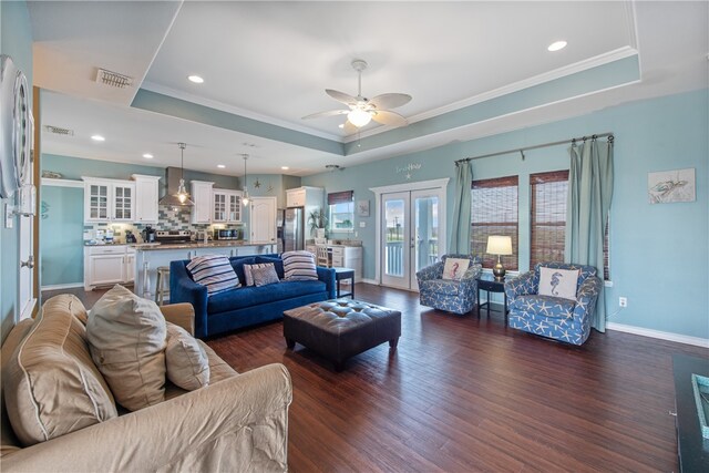 living room featuring dark wood-type flooring, a tray ceiling, ceiling fan, and crown molding