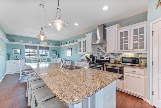 kitchen featuring white cabinetry, appliances with stainless steel finishes, sink, an island with sink, and wall chimney exhaust hood