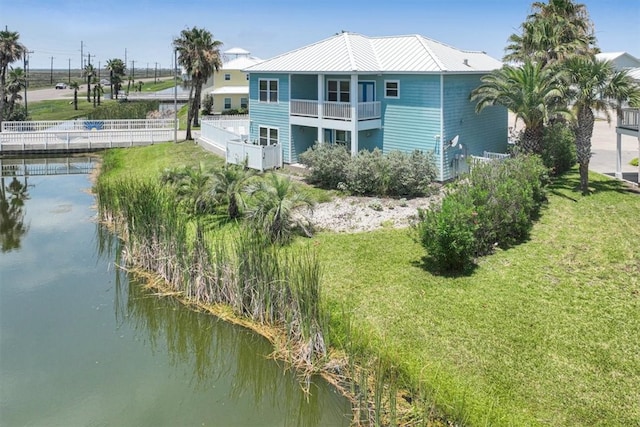 back of house with a water view, a yard, and a balcony