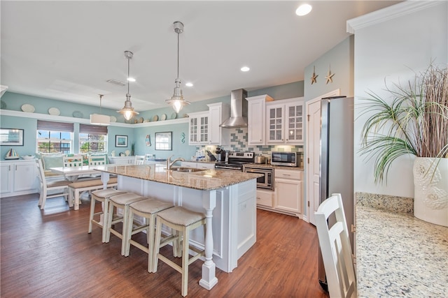 kitchen featuring appliances with stainless steel finishes, dark hardwood / wood-style floors, hanging light fixtures, white cabinets, and wall chimney exhaust hood