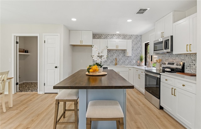 4530 Megal Dr, Corpus Christi, TX 78413 - kitchen with stainless steel appliances, butcher block countertops, light wood finished floors, white cabinets, and a kitchen island