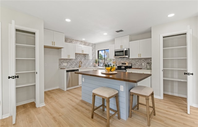 4530 Megal Dr, Corpus Christi, TX 78413 - kitchen with stainless steel appliances, butcher block counters, white cabinets, light wood finished floors, and tasteful backsplash