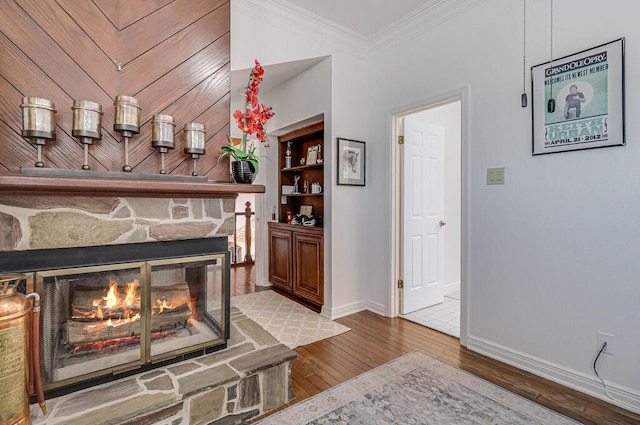 living room with a stone fireplace, wood-type flooring, and crown molding