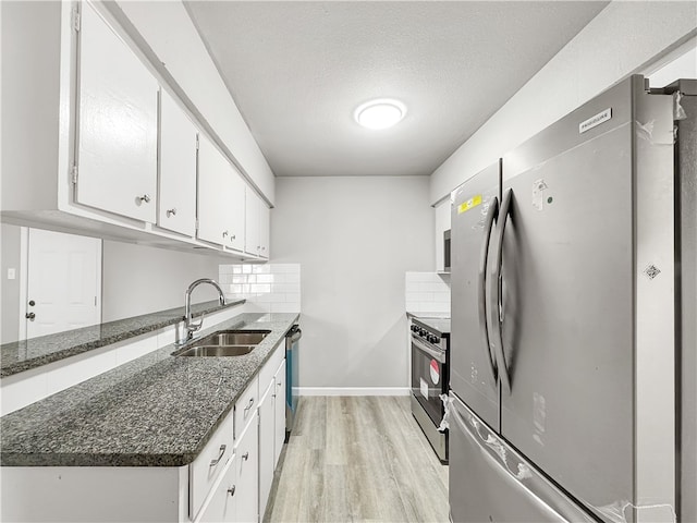 kitchen with sink, appliances with stainless steel finishes, white cabinetry, tasteful backsplash, and dark stone counters